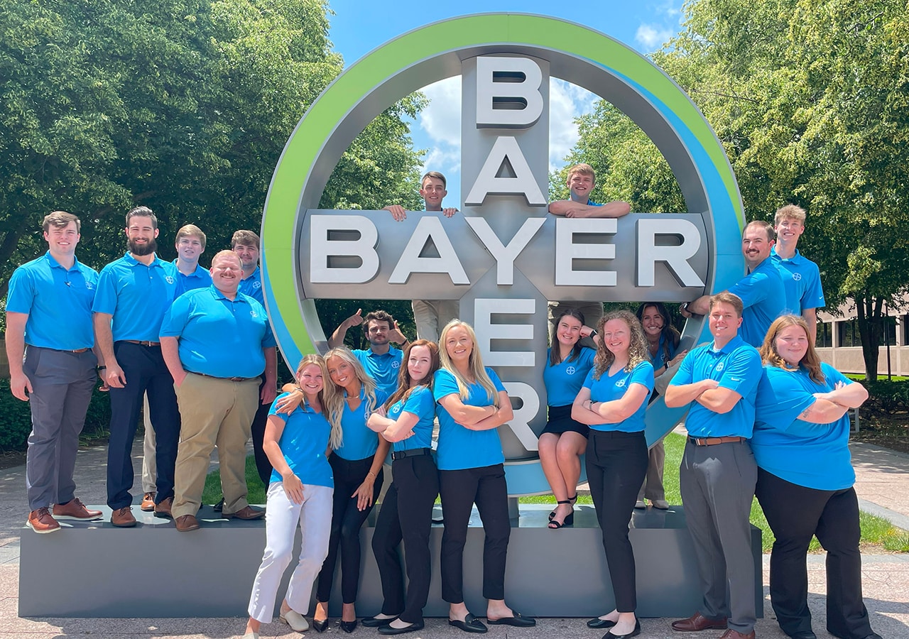 Bayer Interns pose in front of the Bayer sign.